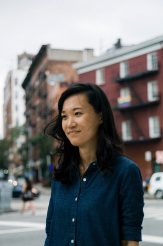 Jenny Xie, an asian woman in a blue shirt with dark hair standing in front of a brick building