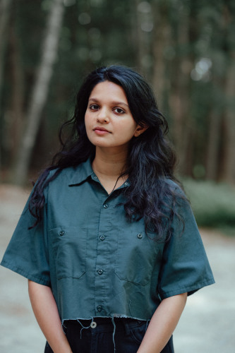 Sarah Thankam Mathews, photo by Ali Reza Malik, courtesy of Macdowell.  A young woman of indian descent with long black hair in a teal shirt standing outside