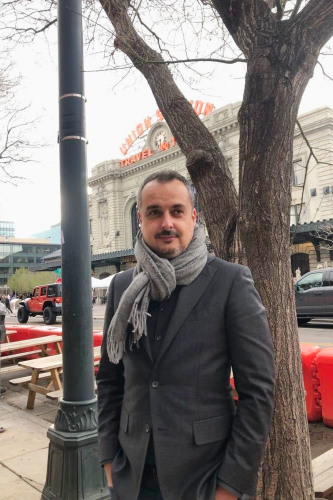 Timothy August. a man standing outside in front of Union Station building. He has a small goatee, gray jacket and large gray scarf around his neck